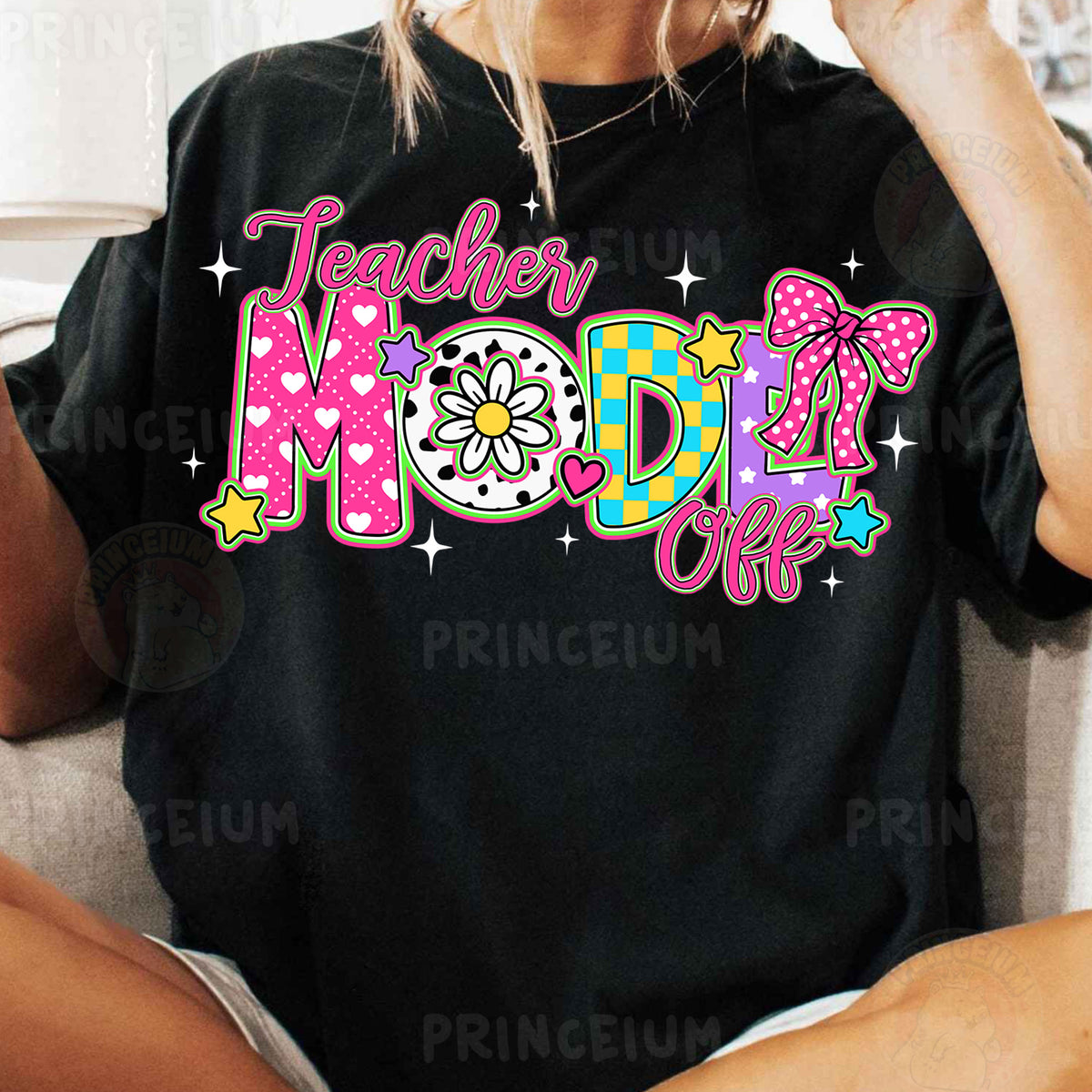 a woman sitting on a couch wearing a black teacher mom shirt