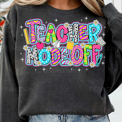 a woman wearing a black teacher sweatshirt with colorful lettering