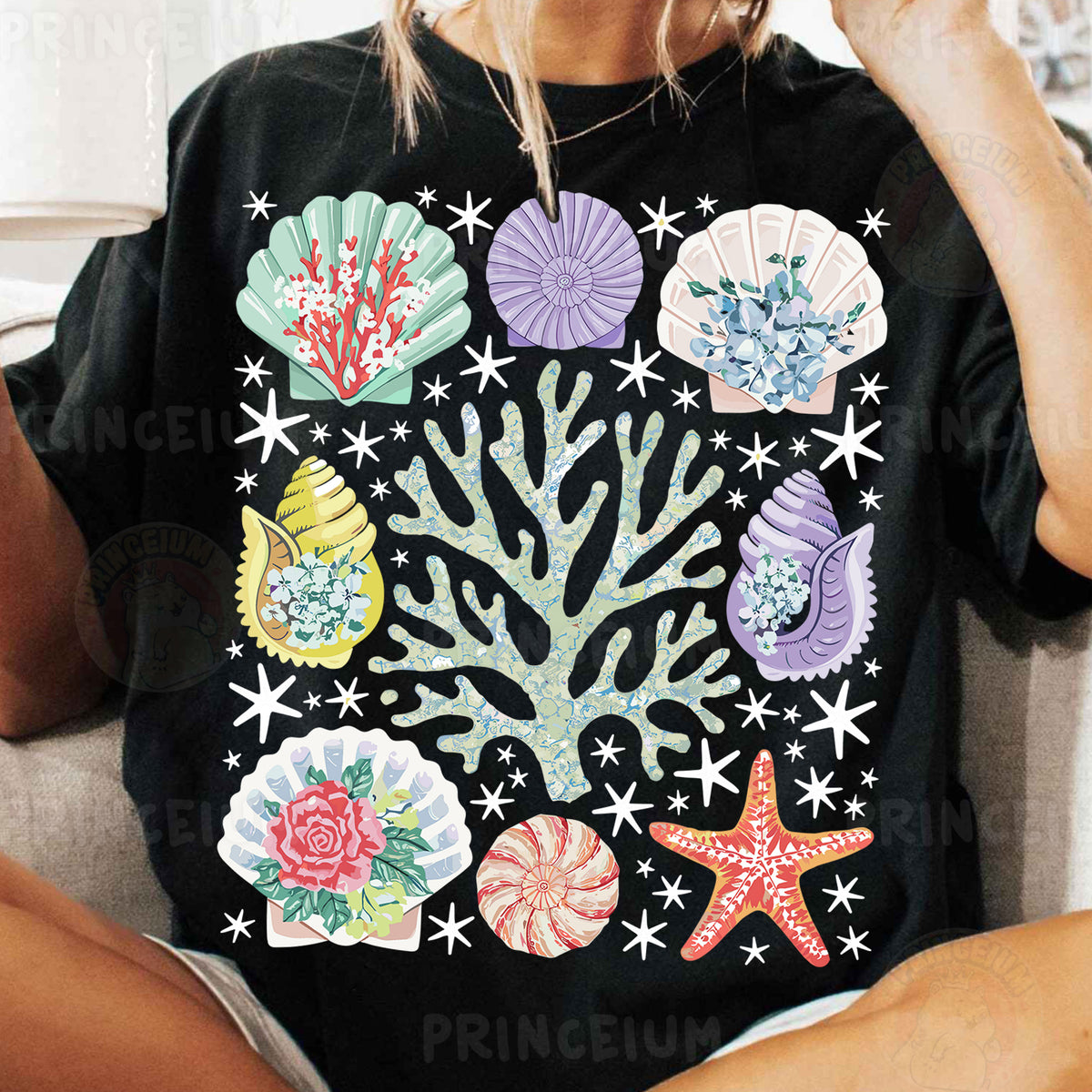 a woman sitting on a couch wearing a black shirt with colorful seashells on