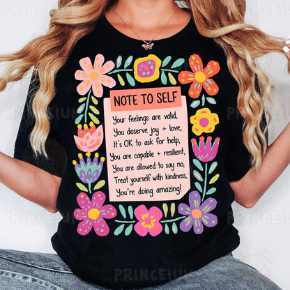 a woman wearing a black t - shirt with flowers and a note to self