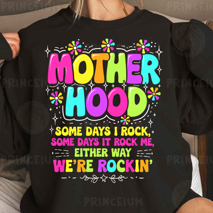 a woman wearing a black sweatshirt that says motherhood some days i rock some days